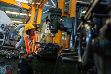 Fototapeta premium Female machinist working with a radial drilling machine in an industrial workshop, wearing a yellow hardhat and reflective vest.