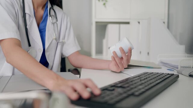 Close up of female doctor holding bottle of medication while using laptop. 