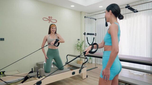 Two young women exercise on Pilates reformer machine in fitness studio.