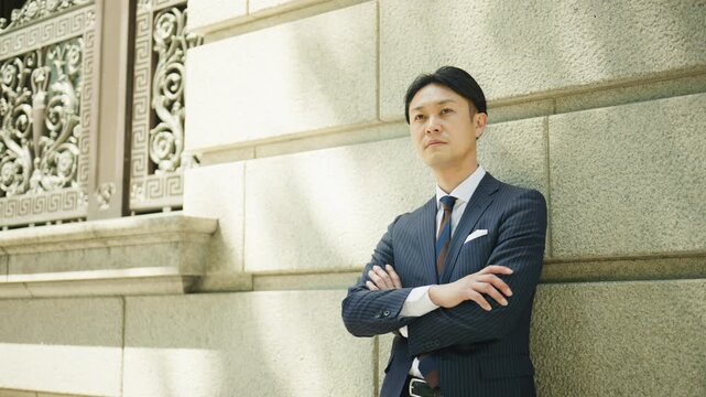 Japanese businessman standing with arms crossed against a stone wall