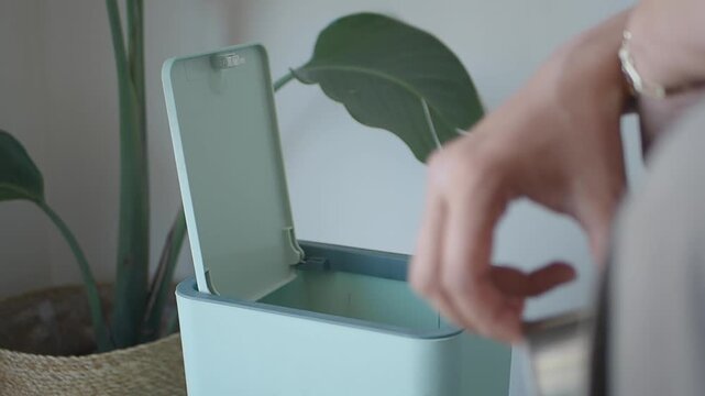 Woman throws away an empty can into a trash bin at home