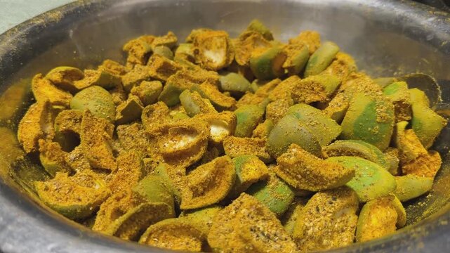 Close up of sliced raw mango pieces thoroughly coated with aromatic dried spices during preparation of traditional Indian mango pickle
