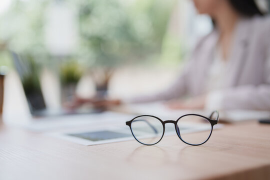 Eyeglasses on office desk with blurred working woman