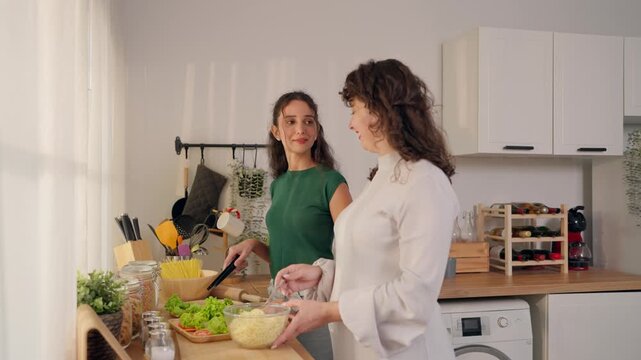 Senior Latino mother cooking with young adult daughter in kitchen at home.