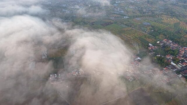 Mist drifts over quiet countryside villages. Fields and rooftops peek through swirling gray haze at Teras Semeru