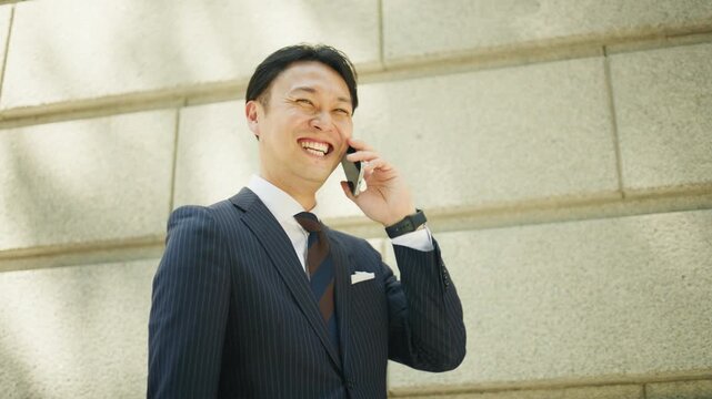 Businessman laughing while holding his smartphone by a stone wall