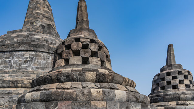 An ancient Hindu temple Candi Borobudur. Architectural details. Stone stupas in the shape of domes with rectangular openings and spires against the backdrop of a blue sky, mandalas. Indonesia.
 