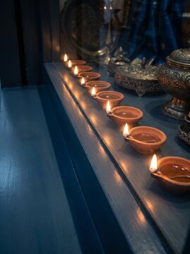 Row of traditional clay oil lamps called diyas glowing with warm flames for Diwali festival celebration, decorative Indian brass artifacts on dark blue background, spiritual lighting, religious concep