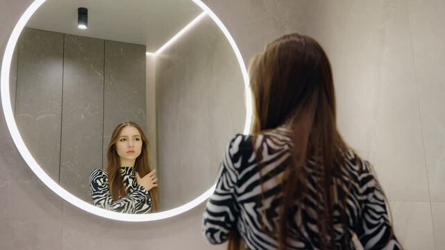 Woman Looking at Her Reflection in an Illuminated Bathroom Mirror