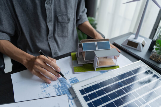 Electrical engineer working on blueprint with solar panel model sustainable energy concept