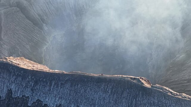 Bromo Crater exhales thick, misty smoke. Rugged, gray stone lines the crater steep edges