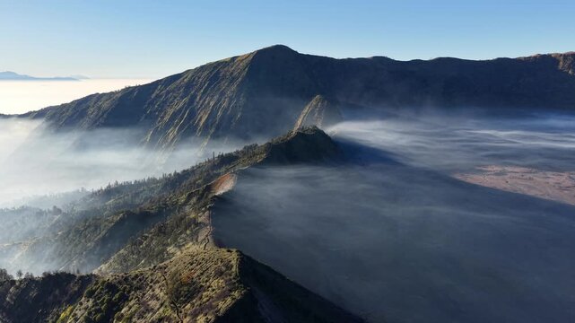Misty morning wraps volcanic peaks. Dense fog drifts over steep mountain ridges near Bromo