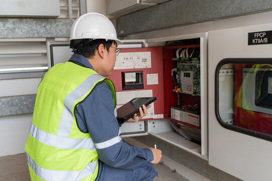 Fire protection system inspection shows a kneeling technician using a tablet beside an open fire alarm panel with visible wiring.