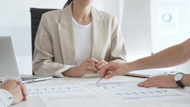 Business team analyzing financial data and discussing marketing strategy during a meeting in the office, businesswoman pointing at charts and explaining strategy to colleagues