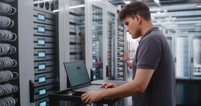 Male System Administrator Analyzes Server Telemetry on Laptop While Female Engineer Works on Nearby Racks, Combining Software Diagnostics with Physical Infrastructure Inspection inside Modern Data
