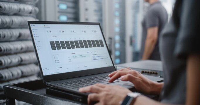 Female Data Center Engineer Monitors Server Telemetry on Laptop, Investigating Critical Overheating Alert While Reviewing Rack Temperatures, Power, Cooling and Network Performance in Real Time.