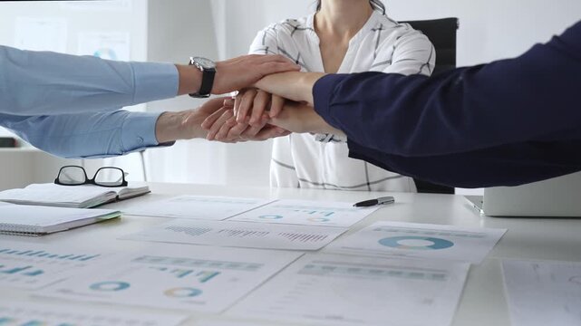 Teamwork and business collaboration with colleagues joining hands over financial charts, symbolizing unity, partnership, success, and strategic corporate planning