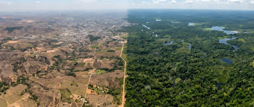 An aerial conceptual landscape contrasting deforested barren land and urban expansion on the left with a lush green tropical rainforest and winding rivers on the right.