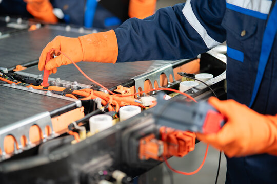 Inside an electric vehicle battery pack a gloved hand presses a red probe onto a terminal beside the insulation tester.