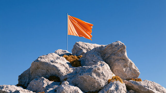Orange flag on rocky mountain summit under clear blue sky with rugged stone texture, strong wind, and minimal outdoor landscape composition