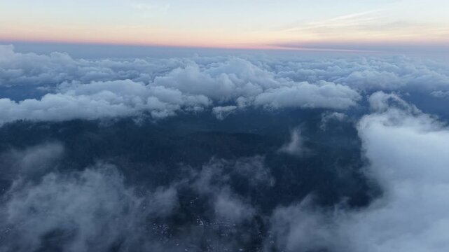 Pastel sunrise above low clouds drifting over misty mountains and a quiet rural village at Pronojiwo, East Java, Indonesia