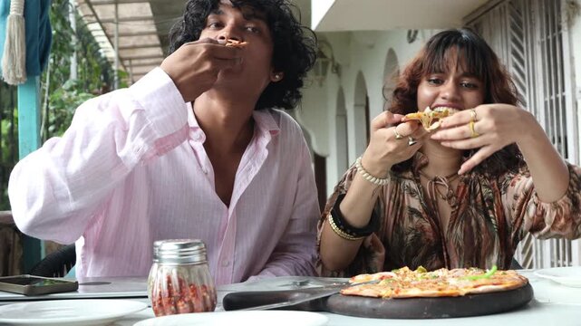 Young Indian Gen Z man and woman enjoying pizza together at a modern caf&eacute;, sharing a casual meal and social moment, friendship, youth lifestyle, urban life in India.