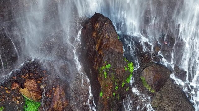 Drone aerial reveal of Tumpak Sewu waterfall plunging over jagged cliffs into misty tropical gorge