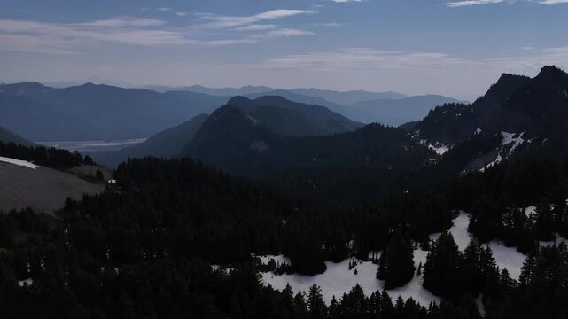 Rugged peaks and evergreen forests of the Cascade Mountains with snow patches under a blue sky 4k aerial drone video