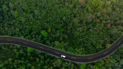 Obraz premium Aerial view of dark green forest road and white electric car Natural landscape and elevated roads Adventure travel and transportation and environmental protection concept 