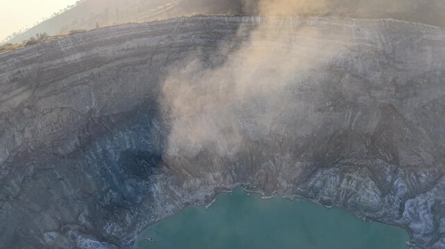 Drone aerial shot of Mount Ijen crater steaming above turquoise acidic lake at sunrise