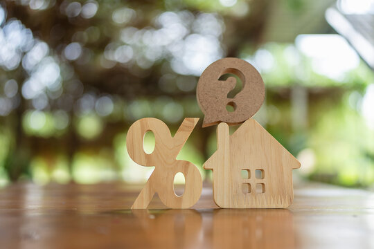 Real estate mortgage and interest rate concept, wooden percentage sign next to house model with question mark bubble on roof, representing property loan inquiry and refinance choice.