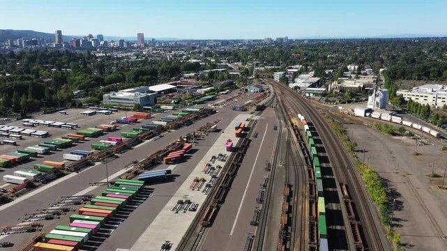 4K aerial drone footage of freight trains and rail yard in Portland, Oregon, USA, with railroad tracks, public transit bus facility, industrial area and downtown skyline in the background