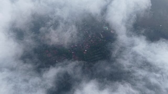 Drone view of Wonosari tea plantation village partially hidden by thick clouds and mist.