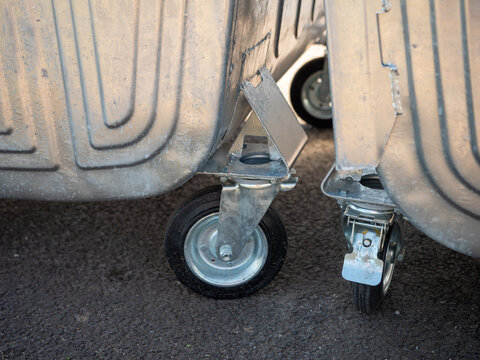 Close-up of heavy-duty caster wheels and wheel brake on galvanized metal waste containers, showing mobility hardware used for moving and securing large garbage bins.