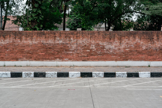 Red brick wall boundary behind a black and white striped curb along a paved concrete parking area.