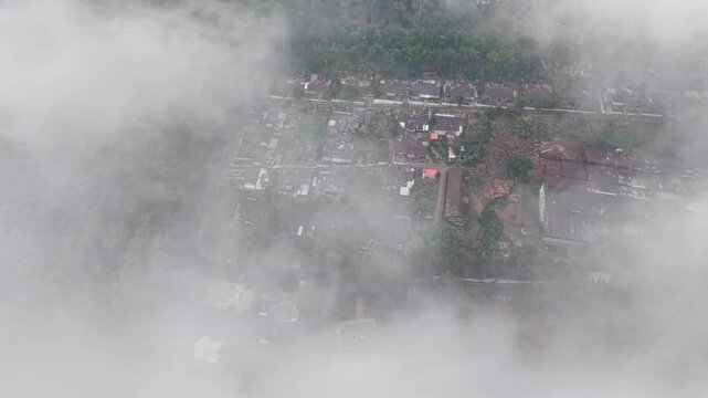 Misty aerial view of Wonosari tea plantation and village framed by terraces and forest.