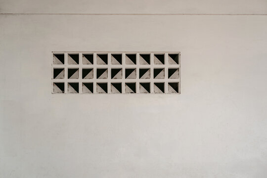 Minimalist architectural detail showing a rectangular ventilation block with geometric triangular patterns built into a plain white wall.