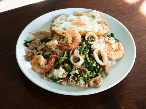 Pad Kaprao, Thai stir-fried holy basil with prawn, squid, chicken and minced pork, served with fried egg and rice
