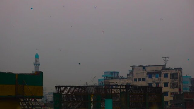 Numerous kites soaring above the urban landscape of Dhaka, Bangladesh, with a mosque minaret visible