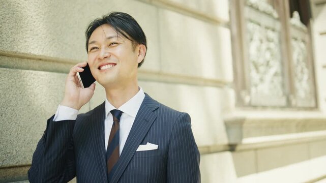 Japanese businessman smiling on a phone call by a stone office building