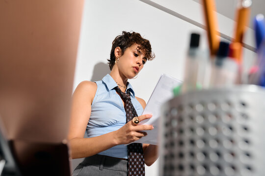 Businesswoman stands in an office space looking at papers.