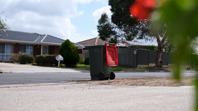 A wheelie bin with an open&nbsp;lid standing empty on a residential kerbside after post-collection waste pickup in&nbsp;a suburban neighborhood. Melbourne, Victoria, Australia