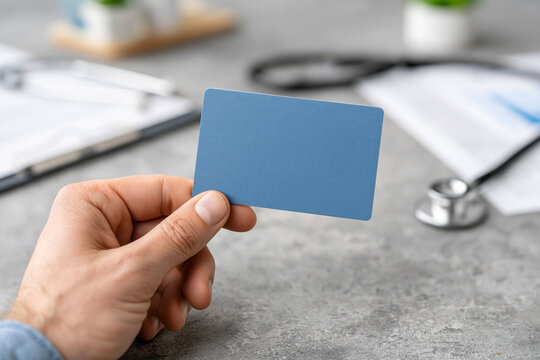 Close-up of hand holding a generic health insurance card beside a stethoscope and medical documents, healthcare coverage and financial protection concept, clean realistic photography