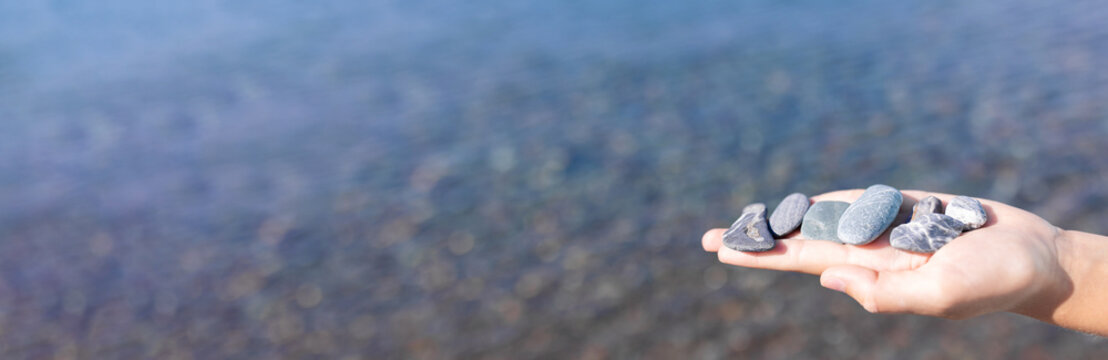 Hand Holding Smooth River Stones With Calm Water Background