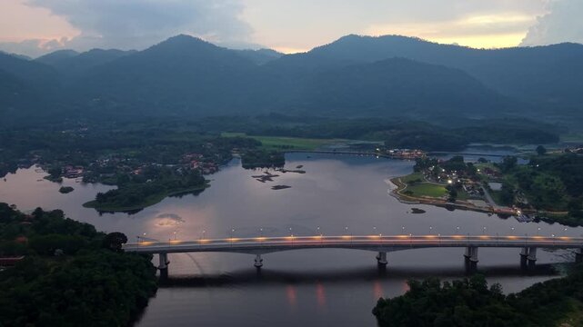 Aerial view of mountains, river, and bridge at golden hour. Sunlight reflects on water at Tasik Raban