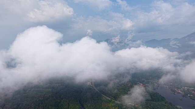 Aerial shot capturing a mist covered forest and river landscape with distant mountains under a cloudy sky at Tasik Raban