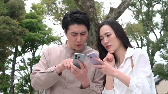 スマートフォンを見て悩むカップル　屋外