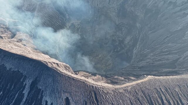 Aerial view of smoking volcano crater. Rugged edges frame steaming, dark interior at Bromo Crater