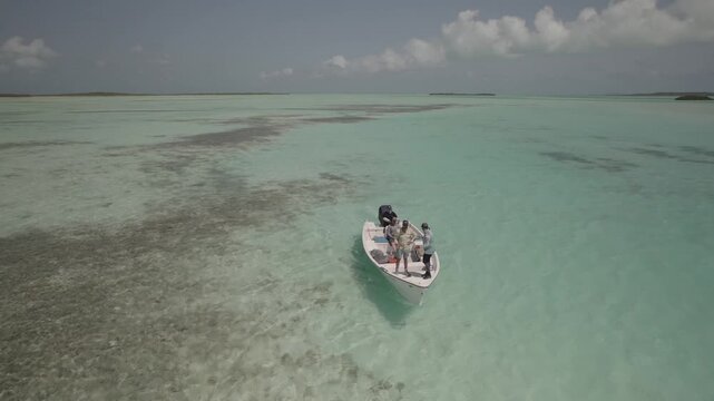 Fishermen exit small boat to wade in shallow clear flats, searching for bonefish