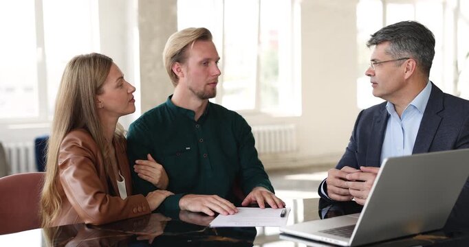 Professional business consultant or bank manager discussing investment contract or mortgage loan with family clients explaining service details reviewing papers and laptop data during office meeting